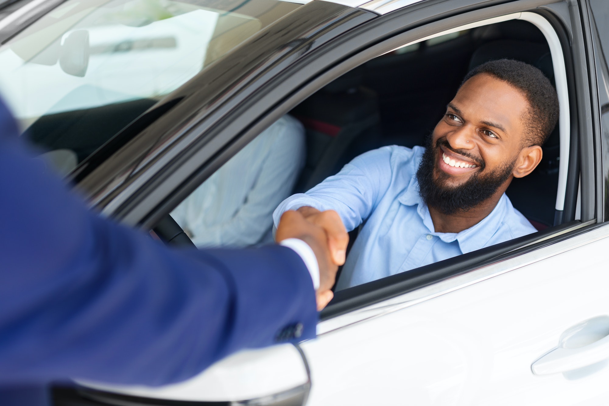 Black Man Sitting Inside Of New Car And Shaking Hands With Salesman