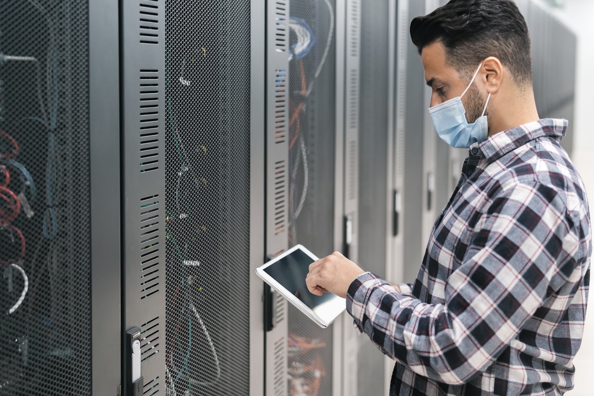 Male informatic engineer working inside server room database while wearing face mask