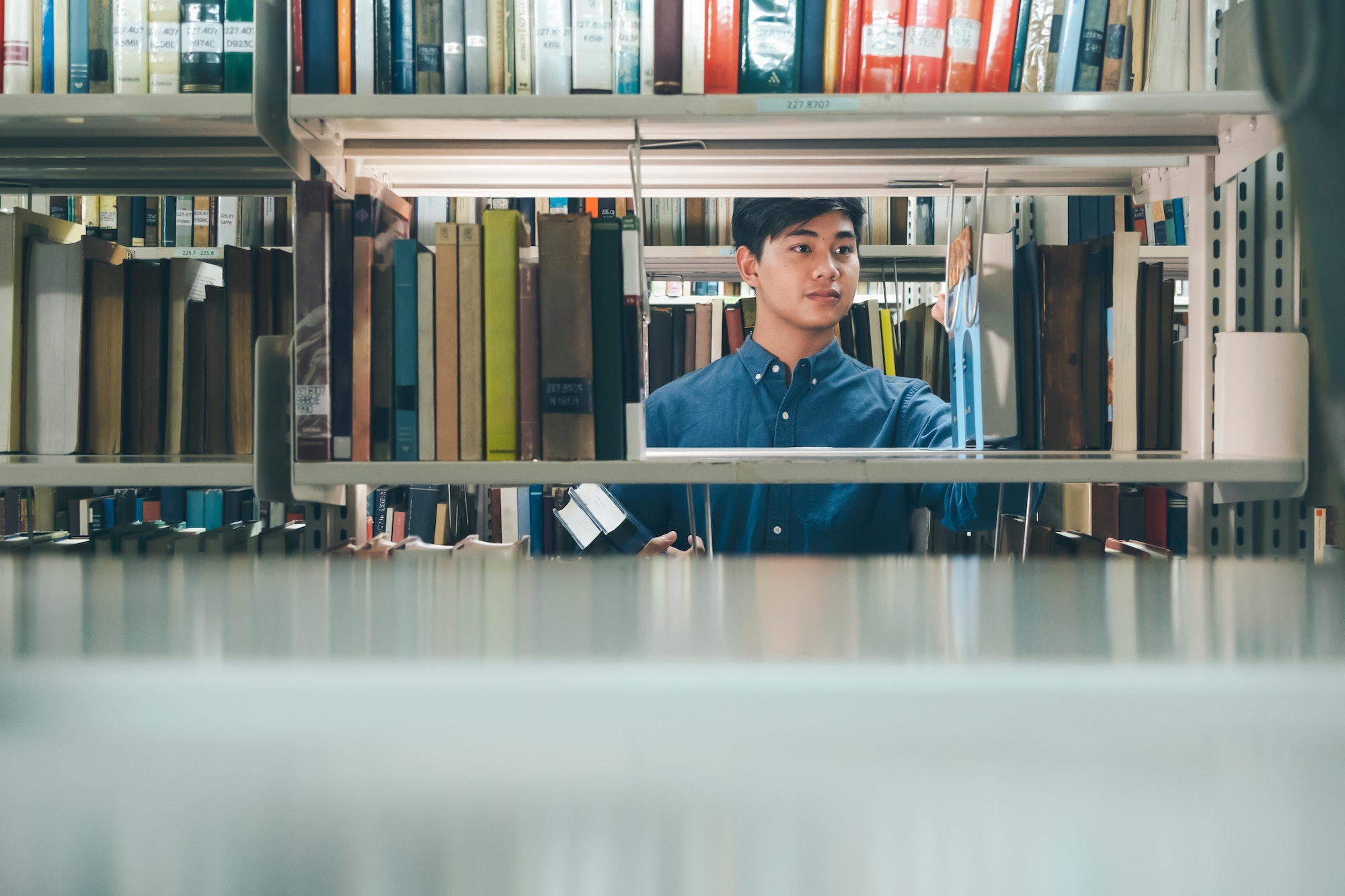 Asian man university student choosing and picking off book from bookshelf in college library for