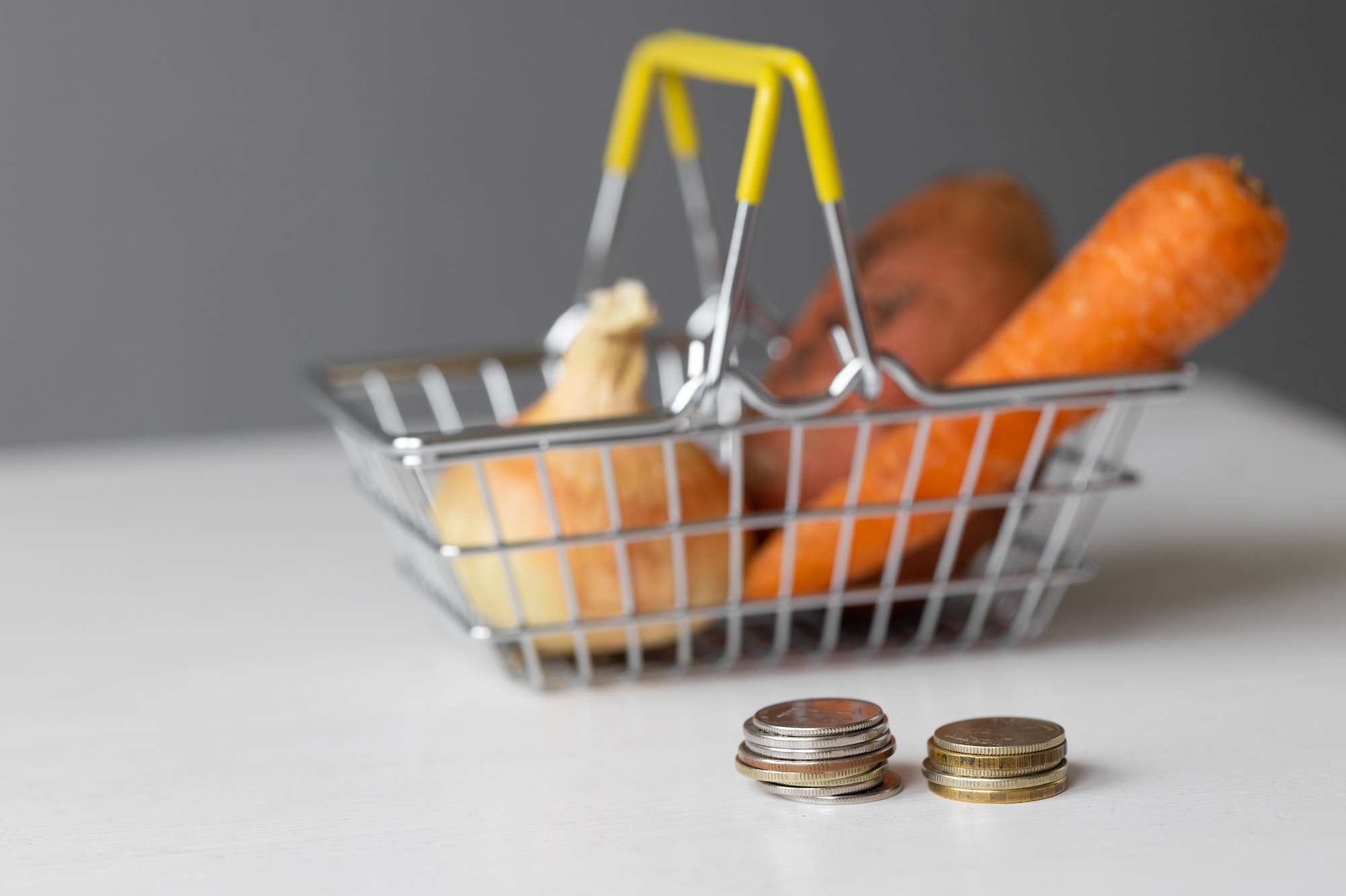 metal supermarket food basket with vegetables and paper money and coins on a white table