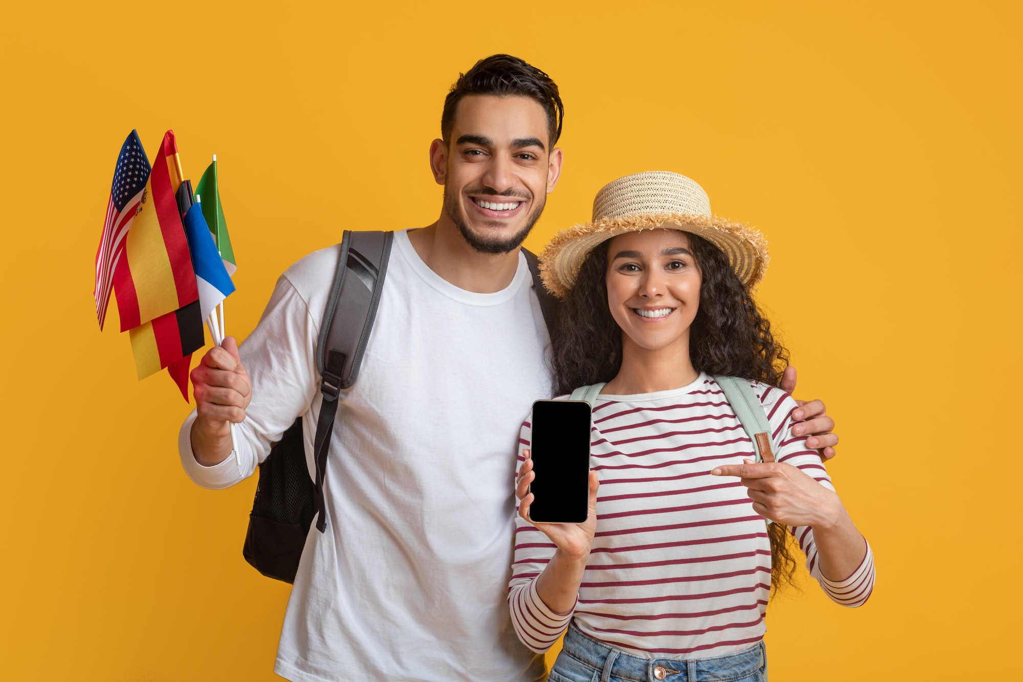 Online Translator App. Happy Young Couple Holding International Flags And Blank Smartphone