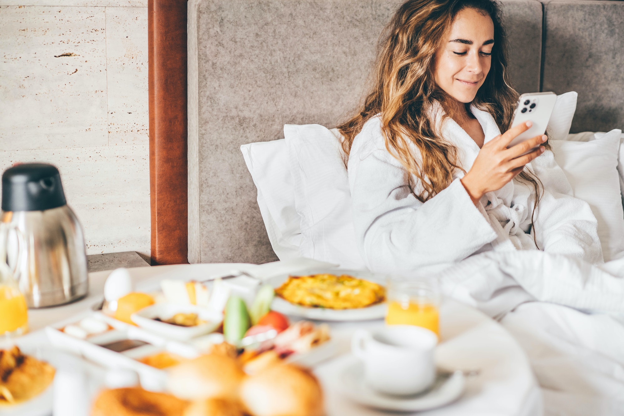 Woman eating breakfast and using phone in the hotel room. Room service breakfast in hotel room.