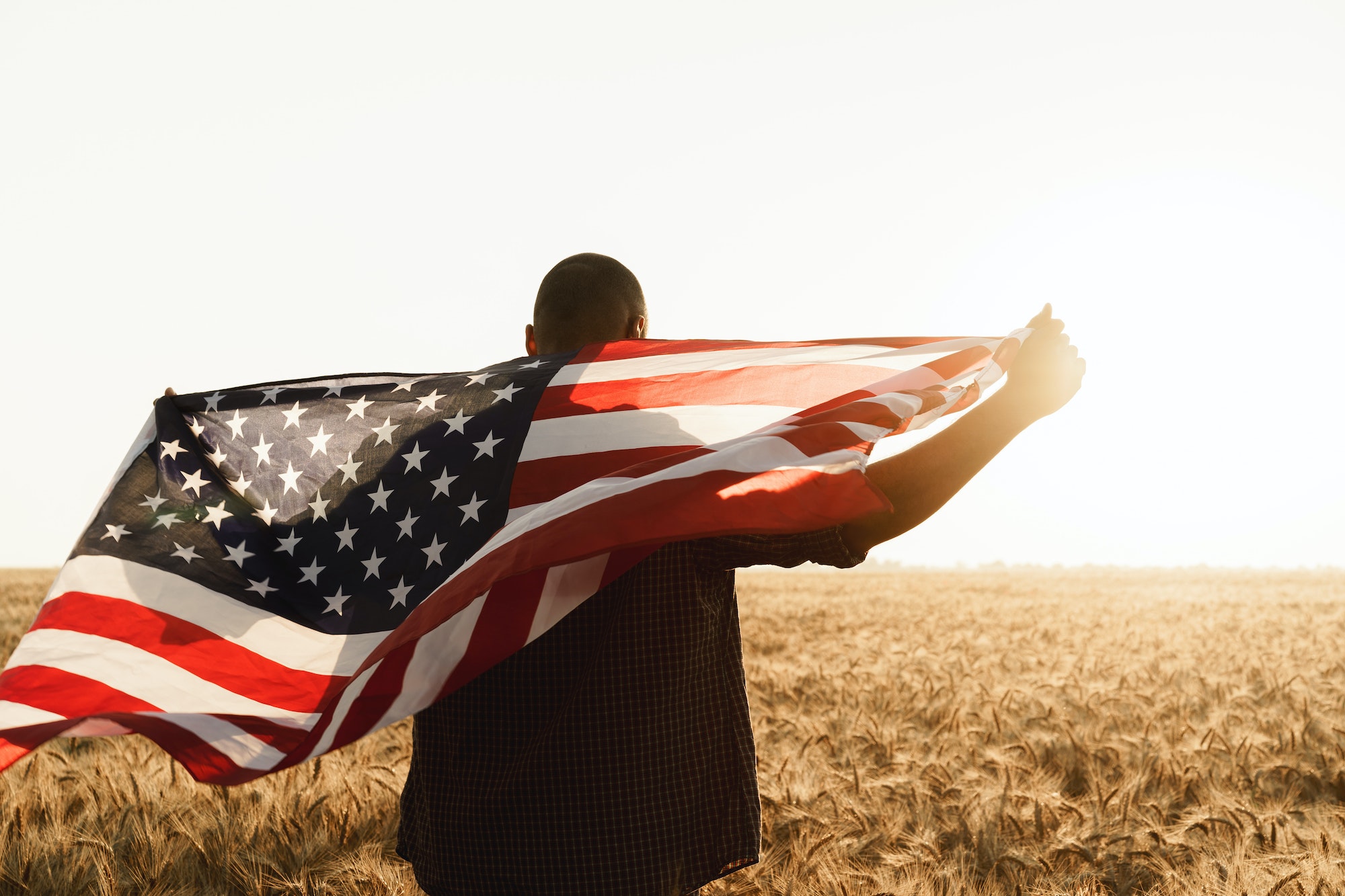 Young man holding American flag on back while standing in wheat field