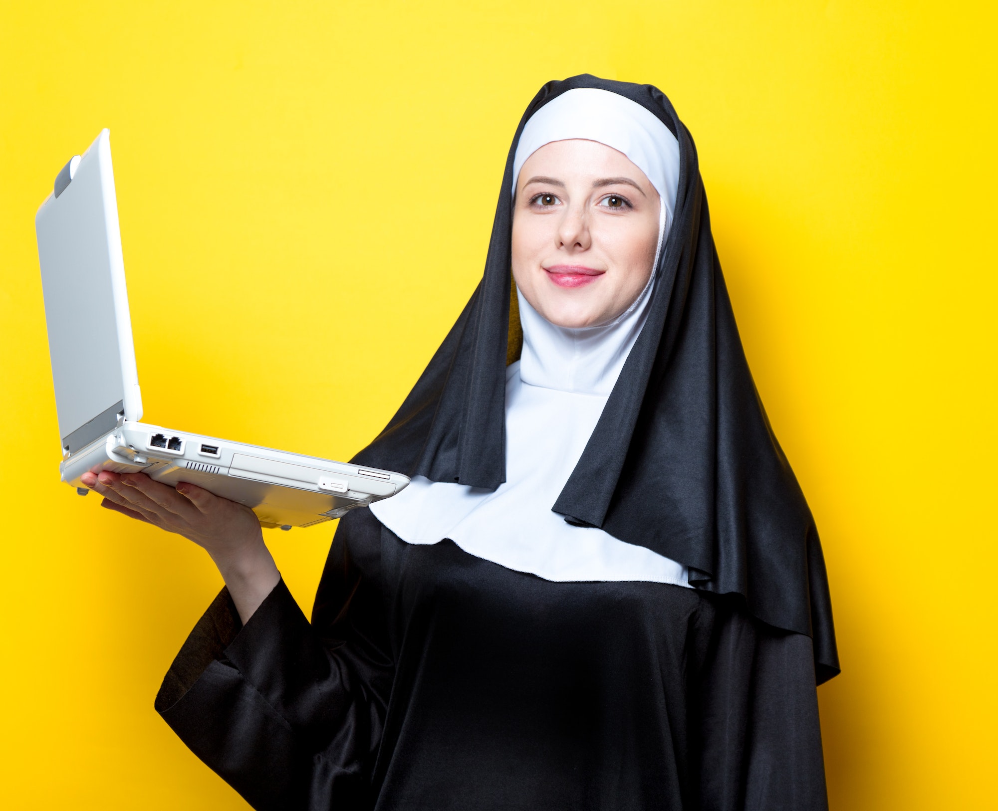 Young smiling nun with white laptop computer